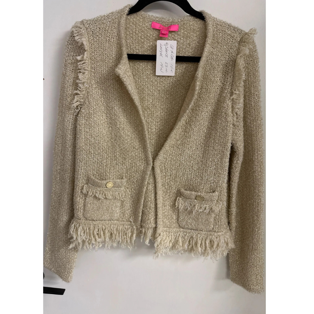 Gold cardigan with fringe details on a hanger against a white background