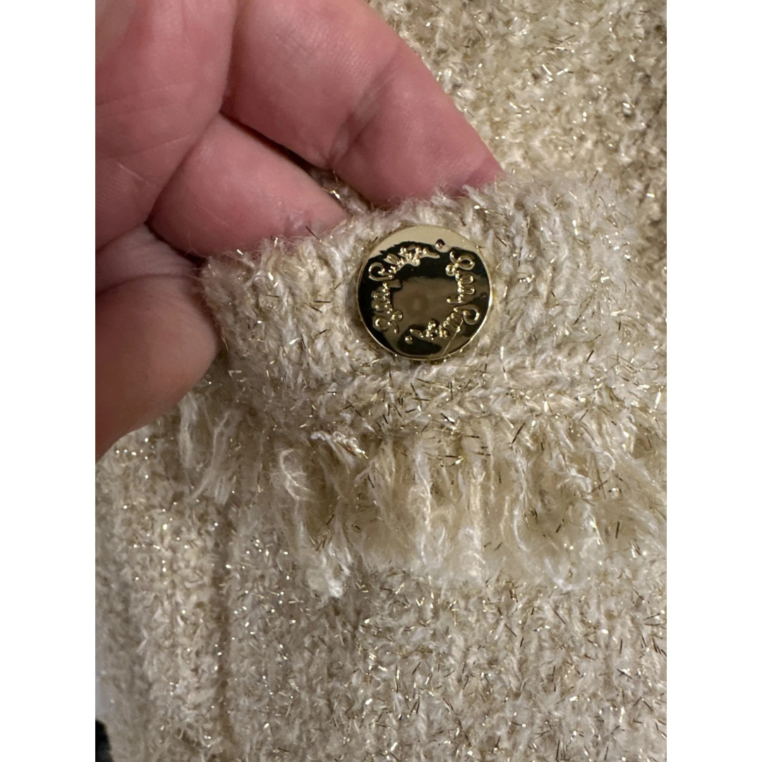 Close-up of a textured gold fabric with a gold button held by a hand.