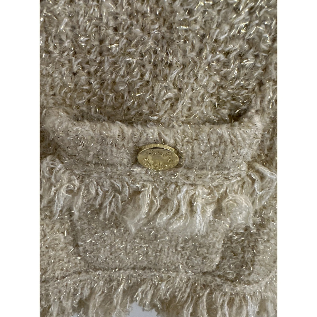 Close-up of a textured Gold fabric with a button and fringes on a white background