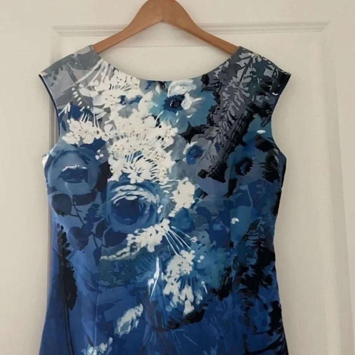 UP close photo upper front of a Blue floral dress on a hanger against a white door