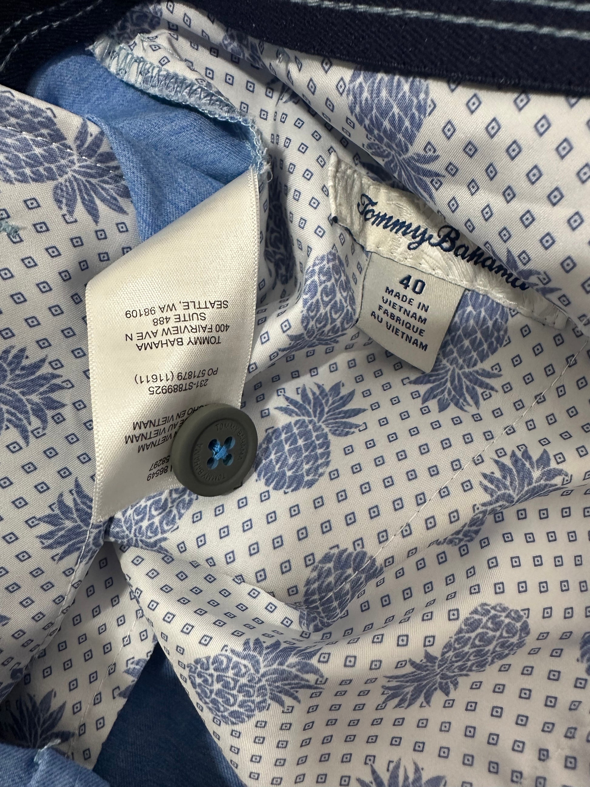 Close-up of a patterned shirt with a button and tag, featuring blue floral designs on a white background.