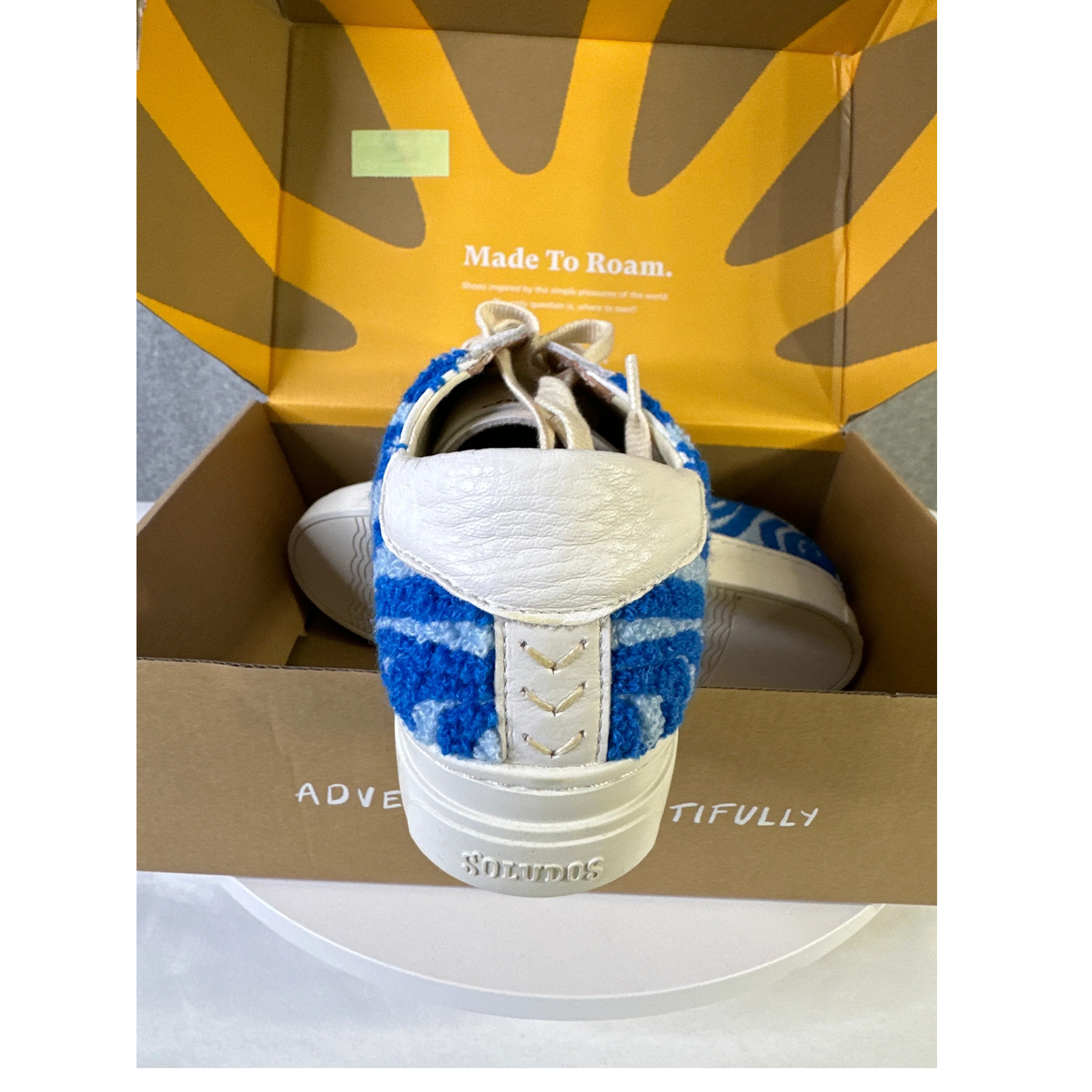 Blue and white sneaker with textured sole in a box, featuring the brand 'Soludos'.