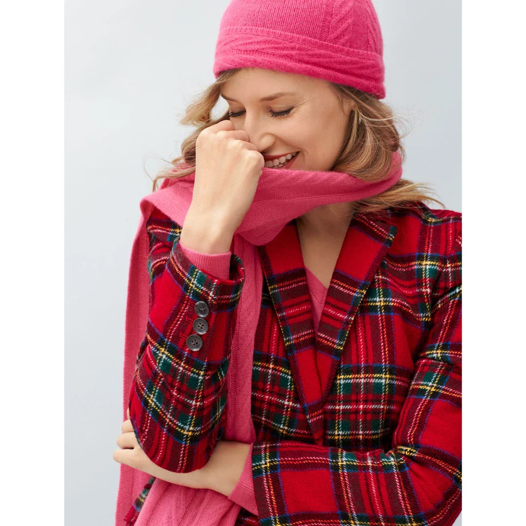 Woman wearing a red plaid coat, pink scarf, and pink beanie against a light gray background
