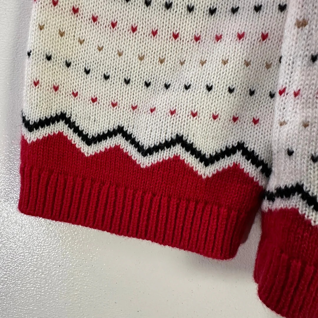 Close-up of a knitted sweater with red cuffs and a patterned design on a white background